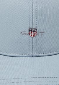 Lys blå baseballcaps med en strukturert krone. Har brodert logo i marineblått, rødt og hvitt. Materialet ser ut til å være teksturert bomull.