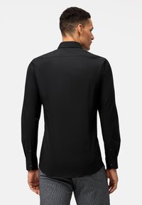 Chemise noire à manches longues avec un col structuré, texture lisse et poignets boutonnés. Présente une coupe ajustée et un design minimaliste.