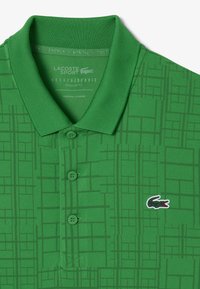 Polo verde con un motivo testurizzato simile all'erba, tre bottoni e un piccolo logo del coccodrillo Lacoste in contrasto. Design di vestibilità regolare.