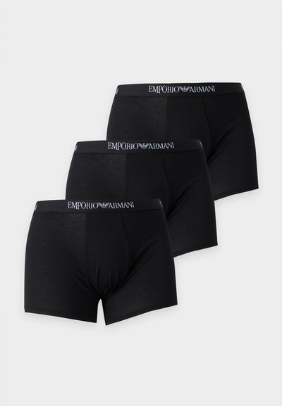Τρία μαύρα ανδρικά μποξεράκια Emporio Armani με λαστιχένια ζώνη με το λογότυπο, τοποθετημένα διαγώνια σε ανοιχτό γκρι φόντο.