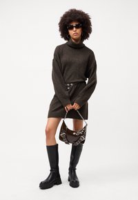 Vestito a dolcevita in maglia marrone scuro con maniche oversize, abbinato a stivali neri fino al ginocchio e una borsa lucida marrone con dettagli metallici.