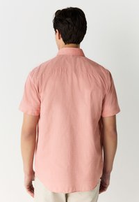 Kortærmet skjorte i lyserødt stof med rygstykke, diskret struktur og buet kant.
