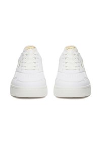 Baltų Reebok batų pora su auksiniu logotipu ant liežuvėlio, matoma iš priekio baltame fone.