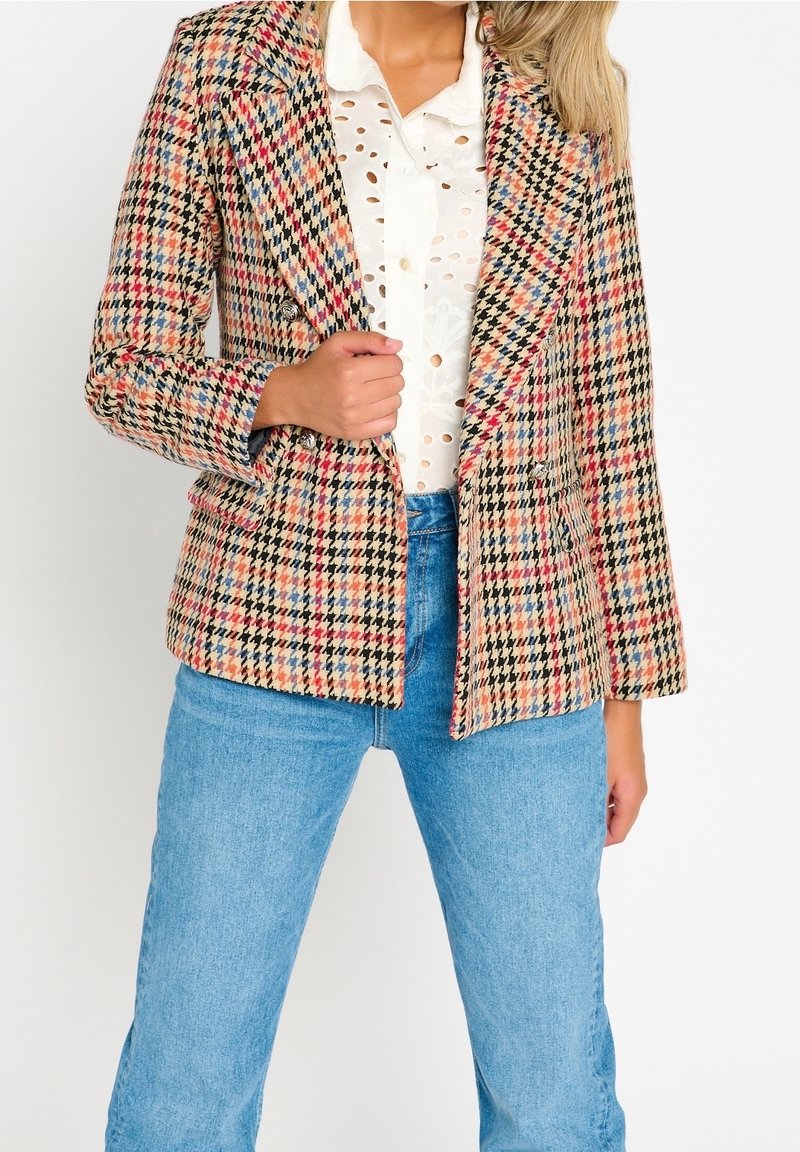 Udekorowana, wielokolorowa marynarka w kratę z wyłogami, podwójnymi guzikami i dwiema przednimi kieszeniami, połączona z białą koszulą i dżinsami.