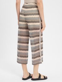 Spodnie z szerokimi nogawkami w zygzakowy wzór w odcieniach beżu, brązu i bieli. Zawierają kontrastowy pasek po bokach oraz fakturowany materiał.