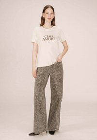 T-shirt crème avec l'inscription "CIAO AMORE" en imprimé marron, associé à un pantalon évasé gris à imprimé léopard et des escarpins noirs à bout pointu.