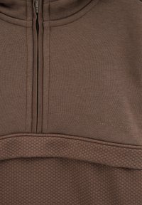 Hnedá mikina na zips s textúrovaným vzorom na dolnej časti, s vysokým golierom a jemným brandingom. Mäkká, pružná tkanina.