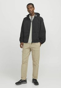 Sort letvægtsjakke med hætte, forlommer, parret med lyse beige cargo bukser og sorte træningssko. Rent, minimalistisk design.