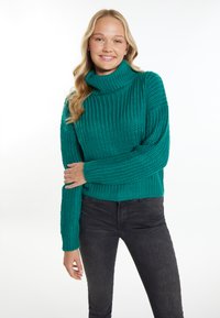 Pulover tricotat teal cu guler înalt, textură cu nervuri și croială lejeră, asortat cu blugi negri cu croială slim.