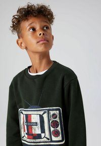 Ciemnozielona bluza z nadrukiem starego telewizora z napisem "BRAK SYGNAŁU", czerwonymi i białymi akcentami oraz teksturowanym wykończeniem.