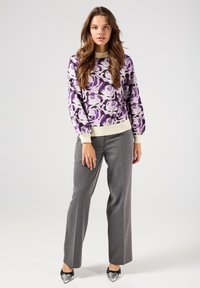 Maglione a maglia floreale viola con polsini a coste crema, abbinato a pantaloni grigi su misura e scarpe nere a punta con dettagli a forma di cuore.