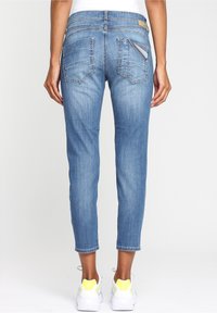 Bakomvy av en person som bär beskurna blå denimjeans och vita sneakers med gula accenter mot vit bakgrund.