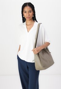 Witte, kortemouw v-hals top gecombineerd met marineblauwe wijde broek. Model houdt een zachte, olijfgroene handtas vast met een gladde textuur.