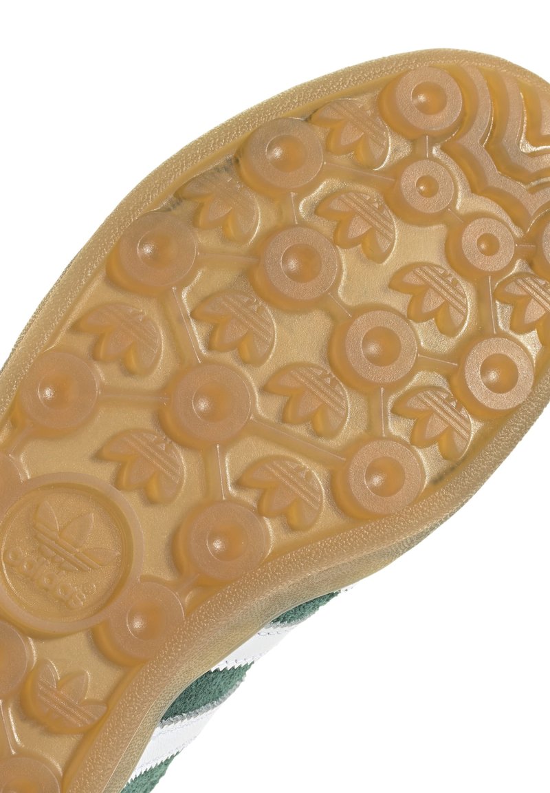 Suola in gomma con motivi circolari e a foglia, con superficie testurizzata; tomaia in suede verde-grigia con strisce bianche.