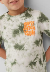 Lichtbeige T-shirt met een groen tie-dye patroon, afgewerkt met een oranje grafische tekst "SURF’S CATCH THE SUN" op de borst. Zacht katoenmateriaal.