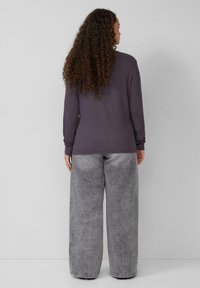 Lange mouwen paarse top met een gestructureerde afwerking, gecombineerd met losse, lichtgrijze jeans met een vervaagd ontwerp en een wijde pijpensilhouet.