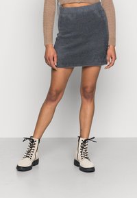 Saia mini de malha cinza com bainha desgastada, combinada com botas em tom creme com atacadores e sola preta robusta.