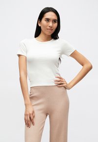 Biele krátke tričko s krátkym rukávom, priliehavé, vyrobené z rebrovanej bavlny, so zaobleným výstrihom. Nosí sa s béžovými textúrovanými nohavicami s vysokým pásom.