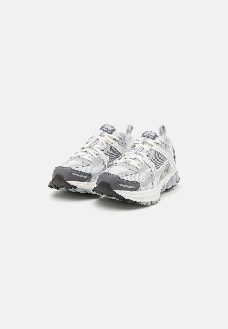 Witte en grijze sportschoenen met een bovenwerk van mesh, ronde neus, gewatteerde kraag en een getextureerde rubberen zool met een opvallend grippatroon.