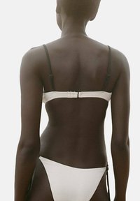 White bikini top with thin black straps and a clasp back; matching white bikini bottoms with side ties, smooth texture.
