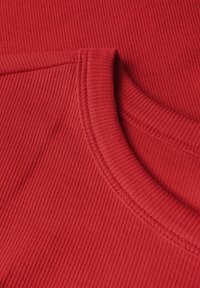 Punainen ribbauskangas, jossa on pyöreä pääntie, esittelee hienoa tekstuuria ja ommeltuja reunoja. Materiaali vaikuttaa pehmeältä ja elastiselta.