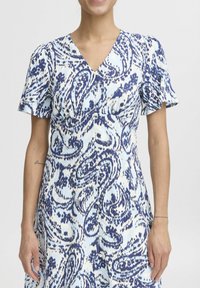 Kratka obleka s kratkimi rokavi in V-izrezom v svetlo modri barvi z mornarsko modrim paisley vzorcem. Ima gumbno zapiranje spredaj in prilegajočo silhueto.