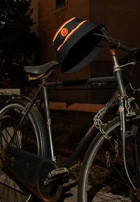 Zwarte bucket hat met gele en rode strepen en een logo, rustend op een vintage fiets met een versleten zadel en een roestig frame.