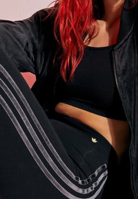 Černý sportovní crop top a legíny se šedými bočními pruhy, které mají malé zlaté logo. Materiál vypadá hladce a je střihově přiléhavý.