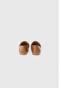 Chaussures slip-on en cuir marron avec une texture lisse et un dos arrondi. Elles comportent un petit détail de boucle sur le côté et une semelle plate couleur tan.