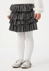 Gonna a balze a righe nere e argento con un design a strati, abbinata a collant bianchi e ballerine argento con un dettaglio a fiocco.