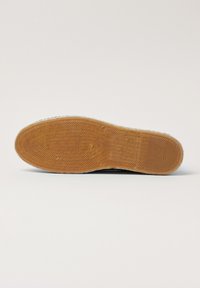 Suela de goma con un patrón de espiga, de color marrón claro y superficie texturizada. Entresuela blanca con marcas de la marca visibles.