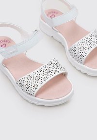 Sandalias blancas con un diseño floral recortado en la correa, plantilla de color rosa claro y suela de goma blanca; correa ajustable para un mejor ajuste.