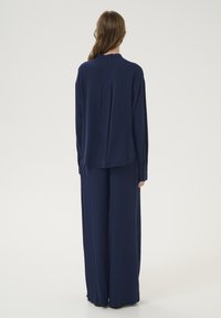 Blusa ampia di colore blu navy e pantaloni a gamba larga realizzati in materiale leggero. Presentano maniche lunghe e un orlo curvo sul retro.