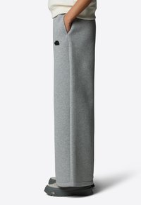 Harmaat verkkahousut rentoa istuvuutta, sivutaskuja ja musta logo lähellä lantioita. Yhdistetty harmaisiin ja mustiin ulkokengiin.