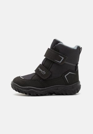 Botas de inverno para crianças pretas, feitas de material textil e sintético, com cintas de velcro e uma sola robusta com um padrão texturizado.