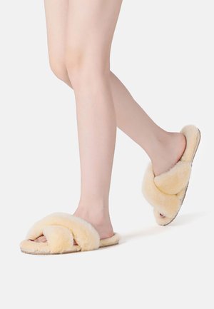 Fuzzy, cream-colored slippers with a cross-strap design and soft texture. Flat sole with a slight natural finish.