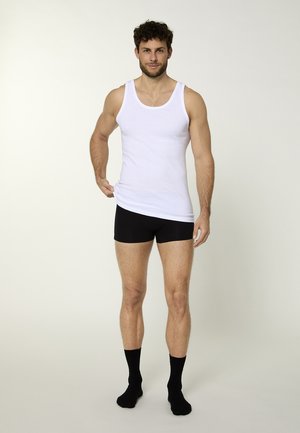 Hvid bomulds tanktop kombineret med sorte shorts og sorte sokker. Tanktoppen har en rund hals; shortsene har en tætsiddende design.