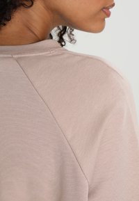 Haut beige clair avec une texture côtelée, doté de manches raglan et d'un col rond lisse. Le tissu semble doux et confortable.