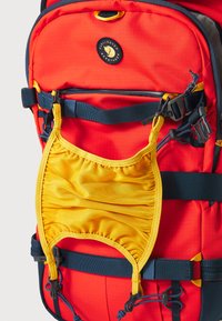 Mochila roja con una tela texturizada, bolsillo elástico amarillo, correas azul marino y herrajes negros para un cierre seguro.