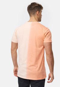 Camiseta de algodón en un degradado de melocotón claro a melocotón más oscuro. Mangas cortas, cuello redondo, textura suave y detalles de costura mínimos.