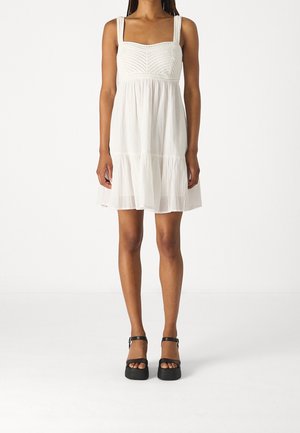 Biała sukienka z kwadratowym dekoltem, plecioną teksturą na gorsecie i warstwową spódnicą. Dobrana do czarnych sandałów na platformie z paskami wokół kostek.