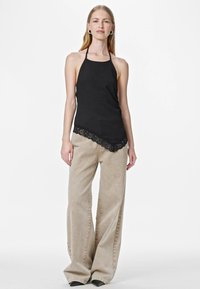 Musta halterneck-toppi, jossa on pitsireunus helmassa, yhdistetty beigen värisiin leveälahkeisiin housuihin. Kankaat ovat sileitä ja kevyitä, mikä luo pehmeän ilmeen.