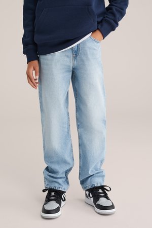Jeans de denim bleu deschis cu o croială relaxată, completate cu un hanorac bleumarin și adidași negri cu gri. Ținută casual cu texturi moi.