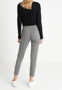 Haut noir à manches longues avec un dos froncé, associé à un pantalon en pied-de-poule gris ajusté et des baskets blanches. Tenue simple et structurée.