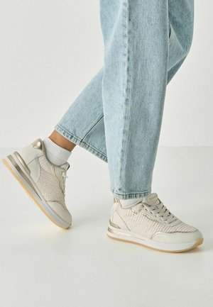 Lichtbeige sneakers met een bovenwerk van mesh en leer, gouden accenten en een gevoerde zool, gecombineerd met lichtblauwe, ontspannen pasvorm jeans.