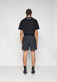 Černé zkrácené tričko s bílým nápisem "HRDÝ BÝT" na zádech, spárované s tmavými šortkami a černými vysokými teniskami. Hladká textura, ležérní střih.