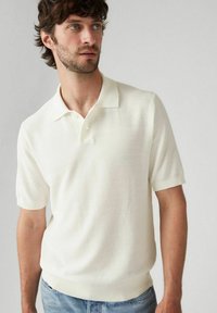 Ljusgräddfärgad kortärmad polo i texturerad stickad tyg med krage, tre knappslå och ribbad fåll och ärmar.