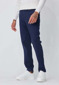 Pantalons couleur bleu marine fuselés en matériau doux, présentant une texture lisse, avec une silhouette épurée et associés à des baskets blanches.