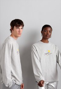 Light gray long-sleeve t-shirts with logo print; relaxed fit; smooth cotton fabric; paired with metallic silver pants; minimalistic design.