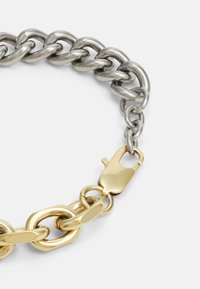 Smycke med kedja i silver- och guldmetall med växlande länkar; har en guld lobsterspänne och släta, polerade ytor.